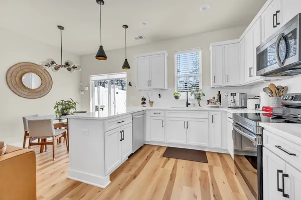 a kitchen with a sink dishwasher a stove a microwave oven and a dining table with wooden floor