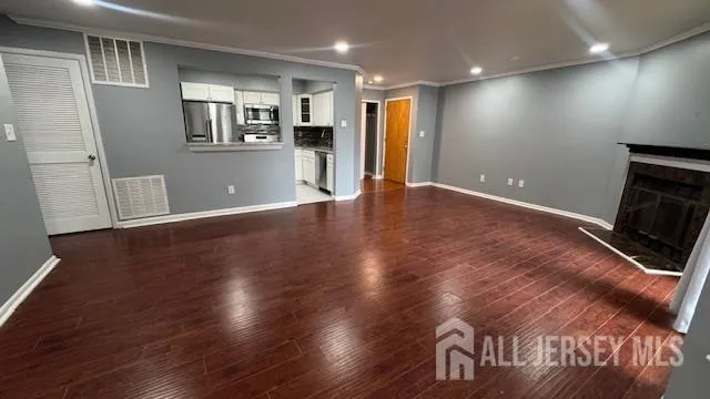 an empty room with wooden floor and kitchen view