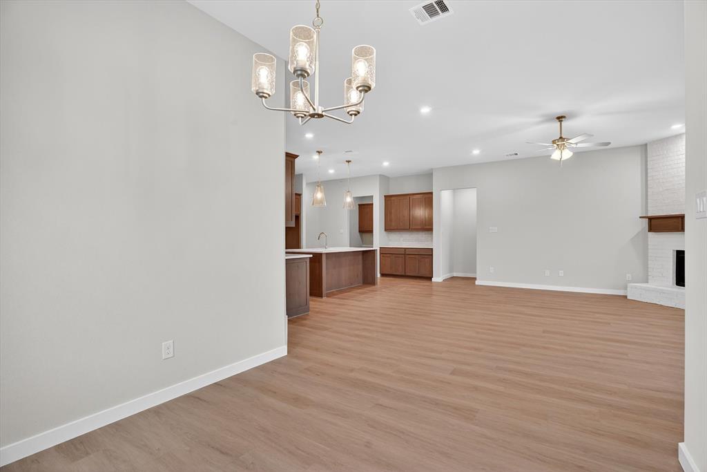 321 Skeen Peak Springtown, TX 76082 - Photo 17 of 37 Open-concept living space featuring wood-finish flooring, a contemporary chandelier, recessed lighting, and a white brick fireplace with a wood mantle
