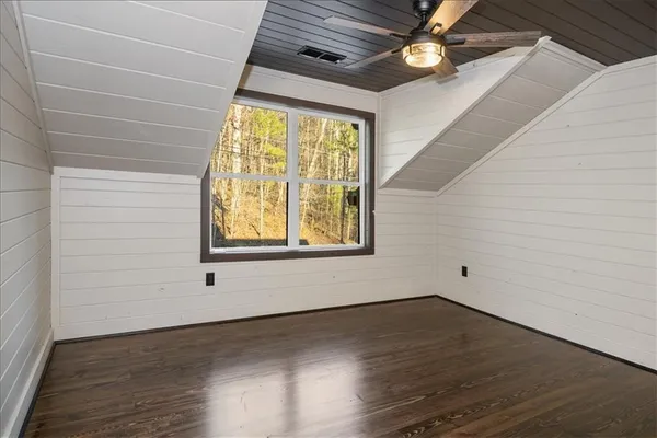 an empty room with wooden floor fan and windows