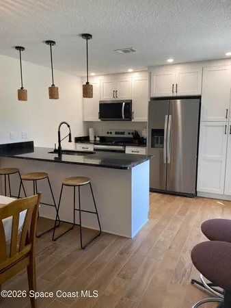 a kitchen with stainless steel appliances granite countertop a stove a sink a refrigerator white cabinets and a dining table