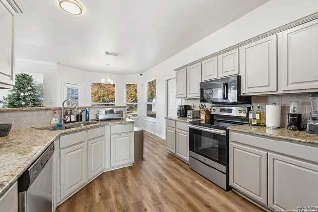 a kitchen with stainless steel appliances granite countertop a sink dishwasher stove and white cabinets with wooden floor