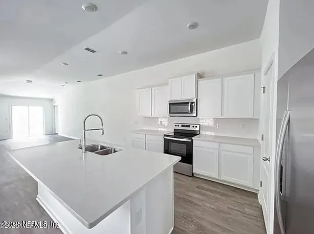 a kitchen with stainless steel appliances a sink a stove a refrigerator cabinets and a window