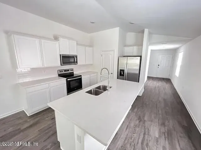 a kitchen with granite countertop a refrigerator a stove top oven a sink dishwasher and white cabinets with wooden floor