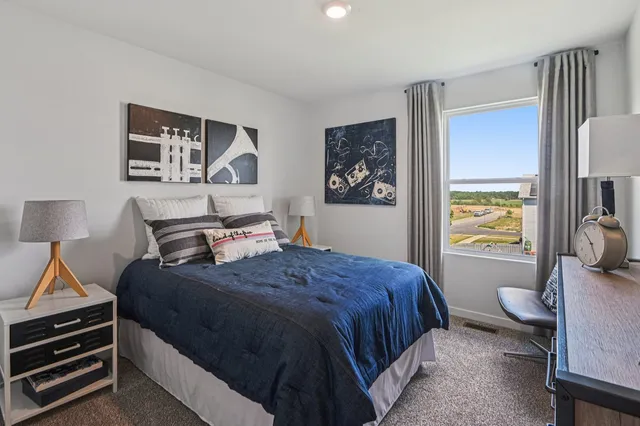 a bedroom with a bed and a lamp on dresser with wooden floor