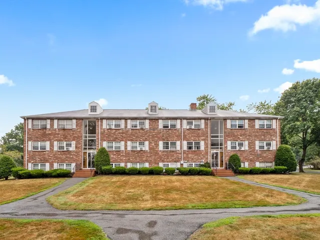 a front view of a building with garden and trees