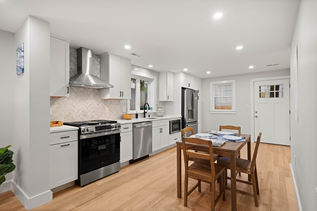 35 Dewey Street, Unit 35 Boston, MA 02125 - Photo 5 of 30 a kitchen with stainless steel appliances kitchen island granite countertop a stove top oven a sink dishwasher a dining table and chairs with wooden floor