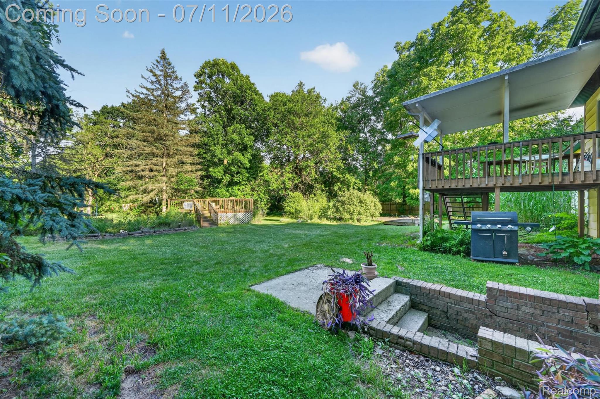 4430 North Center Road Flint, MI 48506 - Photo 41 of 49 Expansive backyard featuring a manicured lawn, established perimeter trees, and a multi-level deck with covered area