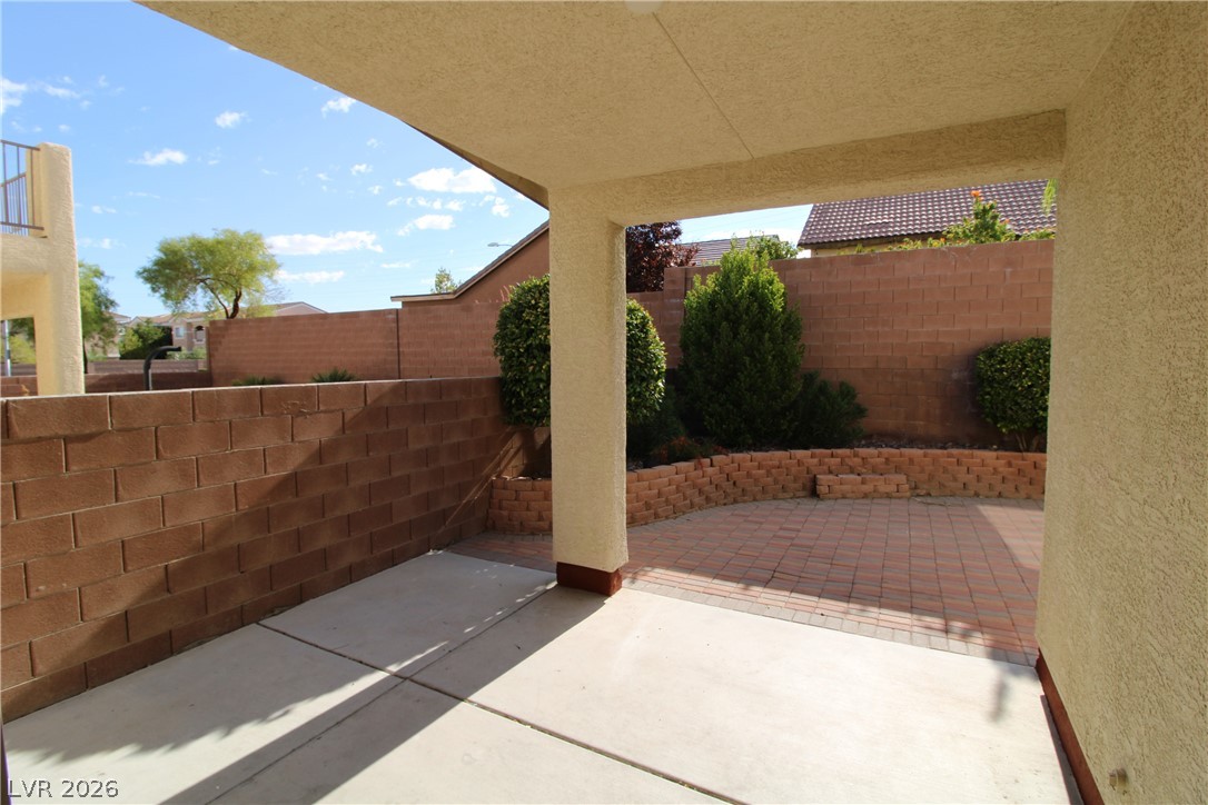 754 Rise Canyon Drive Henderson, NV 89052 - Photo 29 of 34 A covered patio extends to a paver-laid outdoor space, framed by brick fencing and mature landscaping.