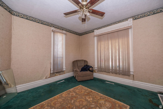 1256 24th Street Ogden, UT 84401 - Photo 5 of 34 Room featuring two windows with vertical blinds, a ceiling fan with light fixture, decorative wallpaper border, and green carpet flooring