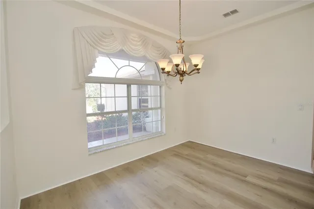 an empty room with wooden floor chandelier and windows