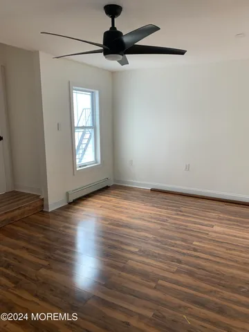 an empty room with wooden floor chandelier fan and windows