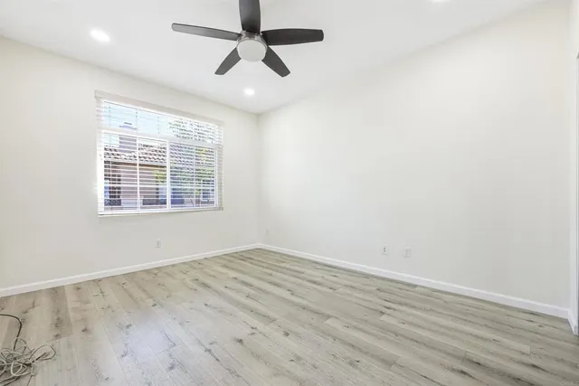 an empty room with wooden floor ceiling fan and windows