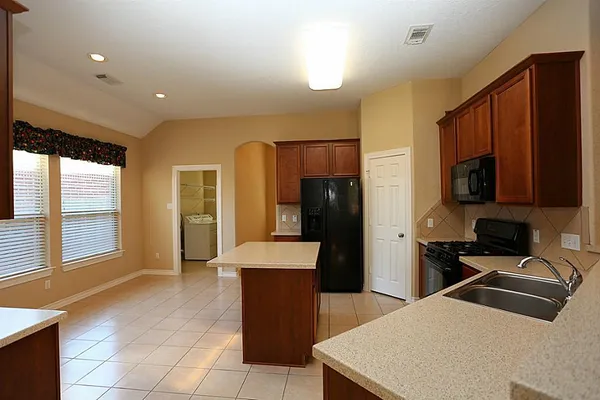 a kitchen with stainless steel appliances kitchen island granite countertop a refrigerator a sink a dining table and chairs with wooden floor