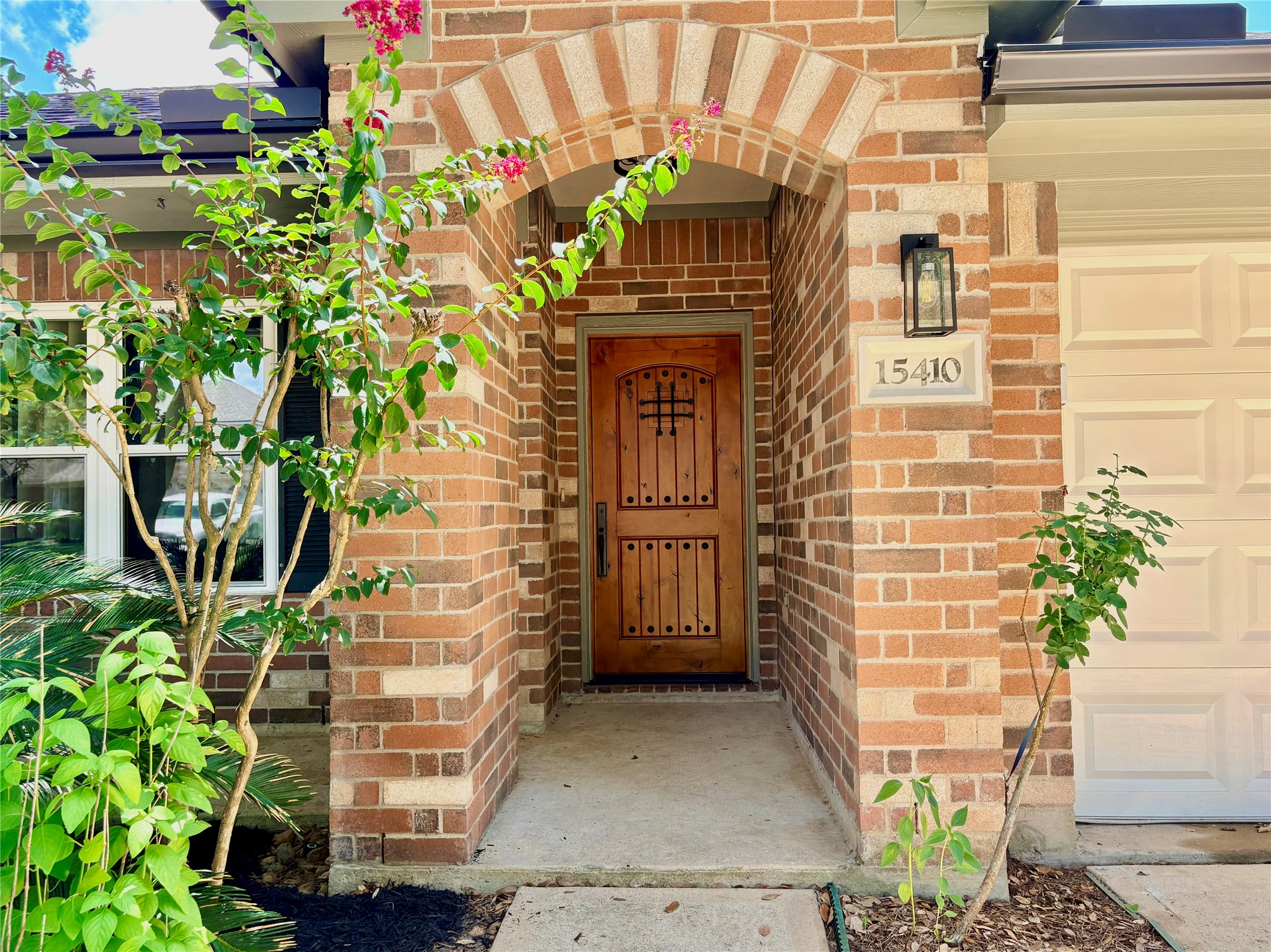 15410 Redbud Berry Way Cypress, TX 77433 - Photo 4 of 49 Charming brick entryway with an arched doorway and wooden door, accented by a lantern-style light fixture. The front is landscaped with greenery, adding a welcoming touch.