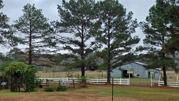 a view of a white house next to a yard with big trees
