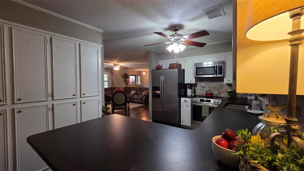 236 Charlie Cannon Road Coushatta, LA 71019 - Photo 30 of 39 Kitchen featuring crown molding, dark countertops, a textured ceiling, appliances with stainless steel finishes, and white cabinetry