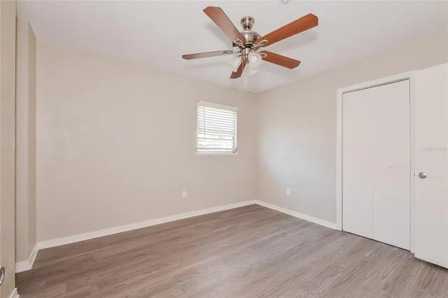 an empty room with wooden floor window and ceiling fan