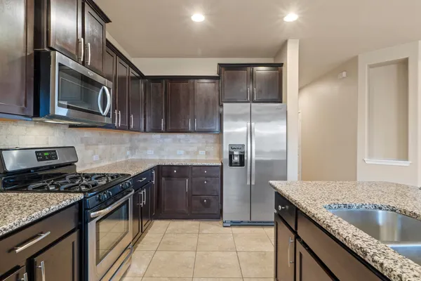 a large kitchen with stainless steel appliances kitchen island granite countertop a refrigerator and a sink