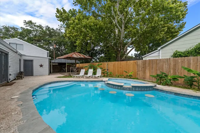 a view of pool with table and chairs under an umbrella with wooden fence