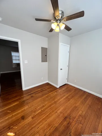 a view of an empty room with wooden floor and a chandelier fan