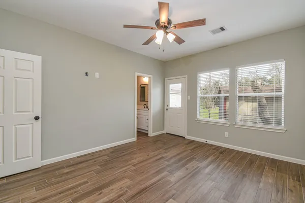 an empty room with wooden floor chandelier fan and windows