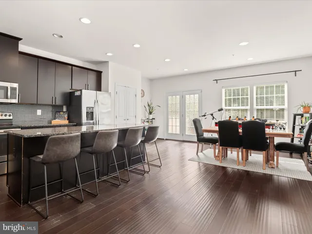 a open dining room with stainless steel appliances kitchen island granite countertop a dining table chairs and a refrigerator