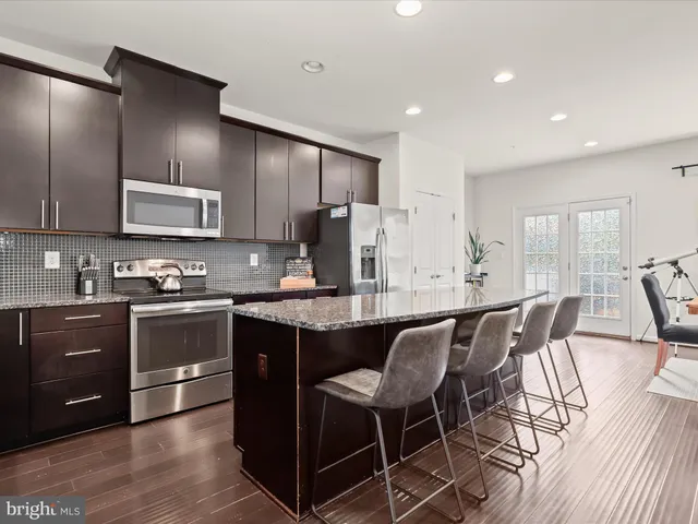 a kitchen with stainless steel appliances granite countertop a stove top oven a sink dishwasher a dining table and chairs with wooden floor