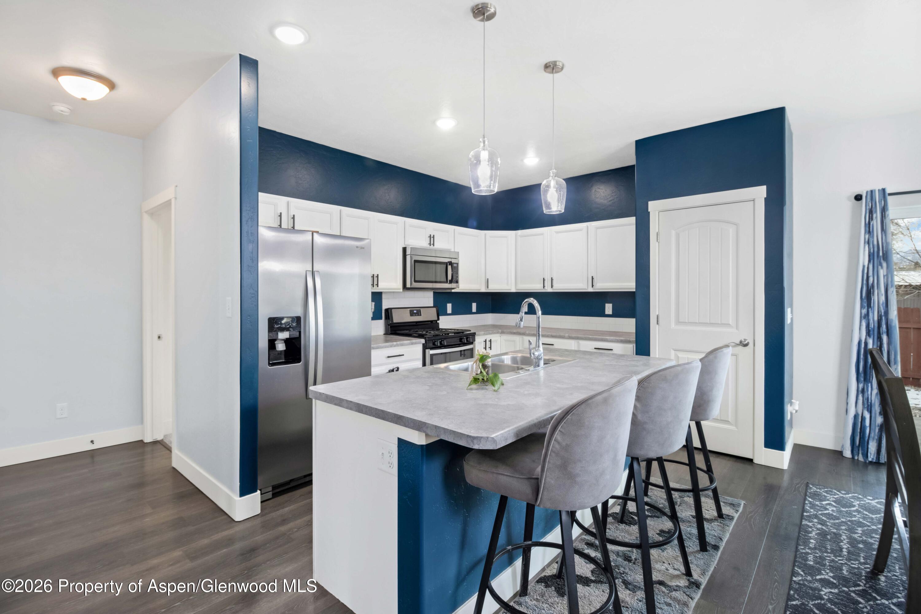 1671 East 17th Circle Rifle, CO 81650 - Photo 3 of 25 a kitchen with stainless steel appliances kitchen island granite countertop a refrigerator a sink a stove a dining table and chairs