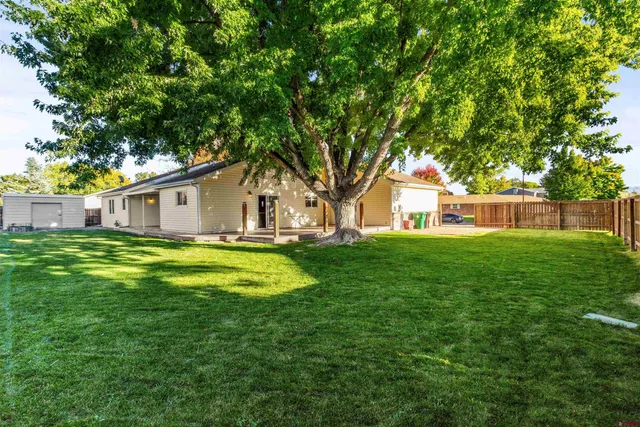 a view of a white house with a big yard plants and large trees