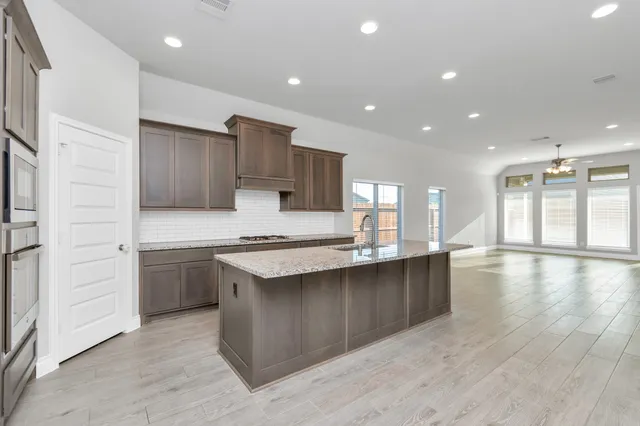 a kitchen with stainless steel appliances granite countertop a stove top oven a sink dishwasher and a refrigerator with wooden floor