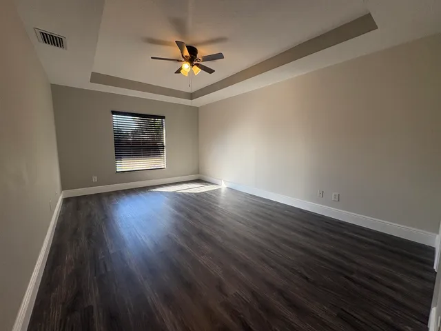 a view of an empty room with wooden floor and a ceiling fan
