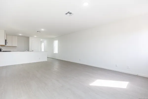 a view of an empty room with kitchen view and window