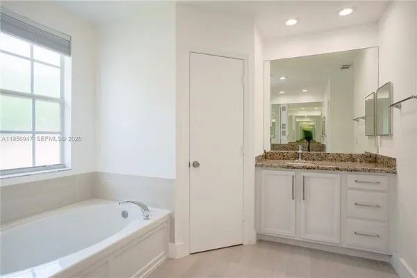 a bathroom with a granite countertop sink a bathtub and a mirror