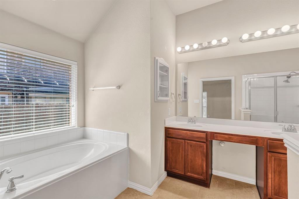 5316 Ridgeson Drive McKinney, TX 75071 - Photo 23 of 33 Bathroom featuring a built-in soaking tub with tiled surround, dual vanity with wood-finish cabinetry, integrated sinks, a large mirror, and a separate glass-enclosed shower with subway tile