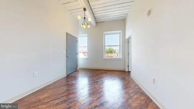 an empty room with wooden floor chandelier and windows