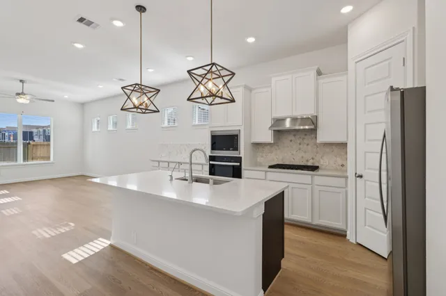 a kitchen with kitchen island granite countertop stainless steel appliances a sink cabinets and a wooden floor