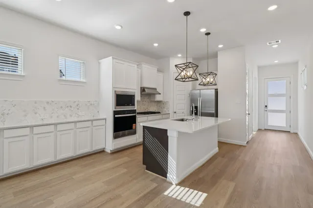a large white kitchen with a center island wooden floor and stainless steel appliances