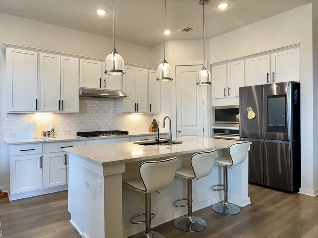 a kitchen with stainless steel appliances granite countertop a sink a stove a refrigerator cabinets and chairs