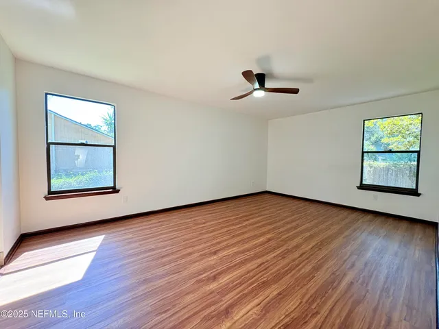 an empty room with wooden floor ceiling fan and windows