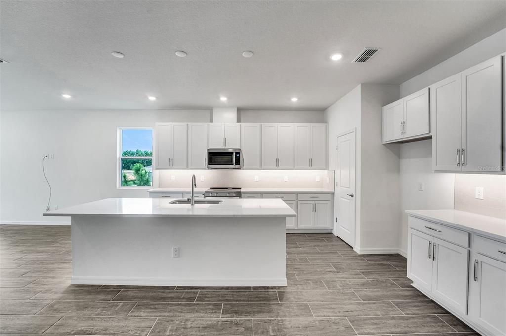 35163 Tuscan Hill Road Dade City, FL 33525 - Photo 21 of 45 a large white kitchen with kitchen island a sink a center island stainless steel appliances and a cabinets