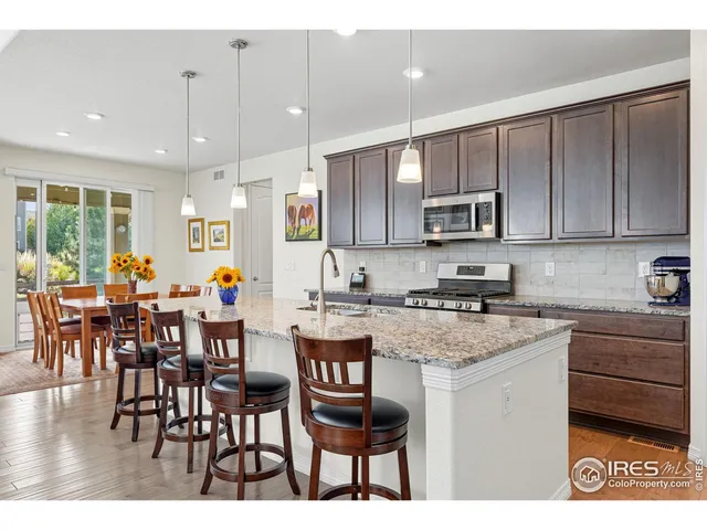 a kitchen with stainless steel appliances granite countertop a stove top oven a sink a refrigerator white cabinets and chairs