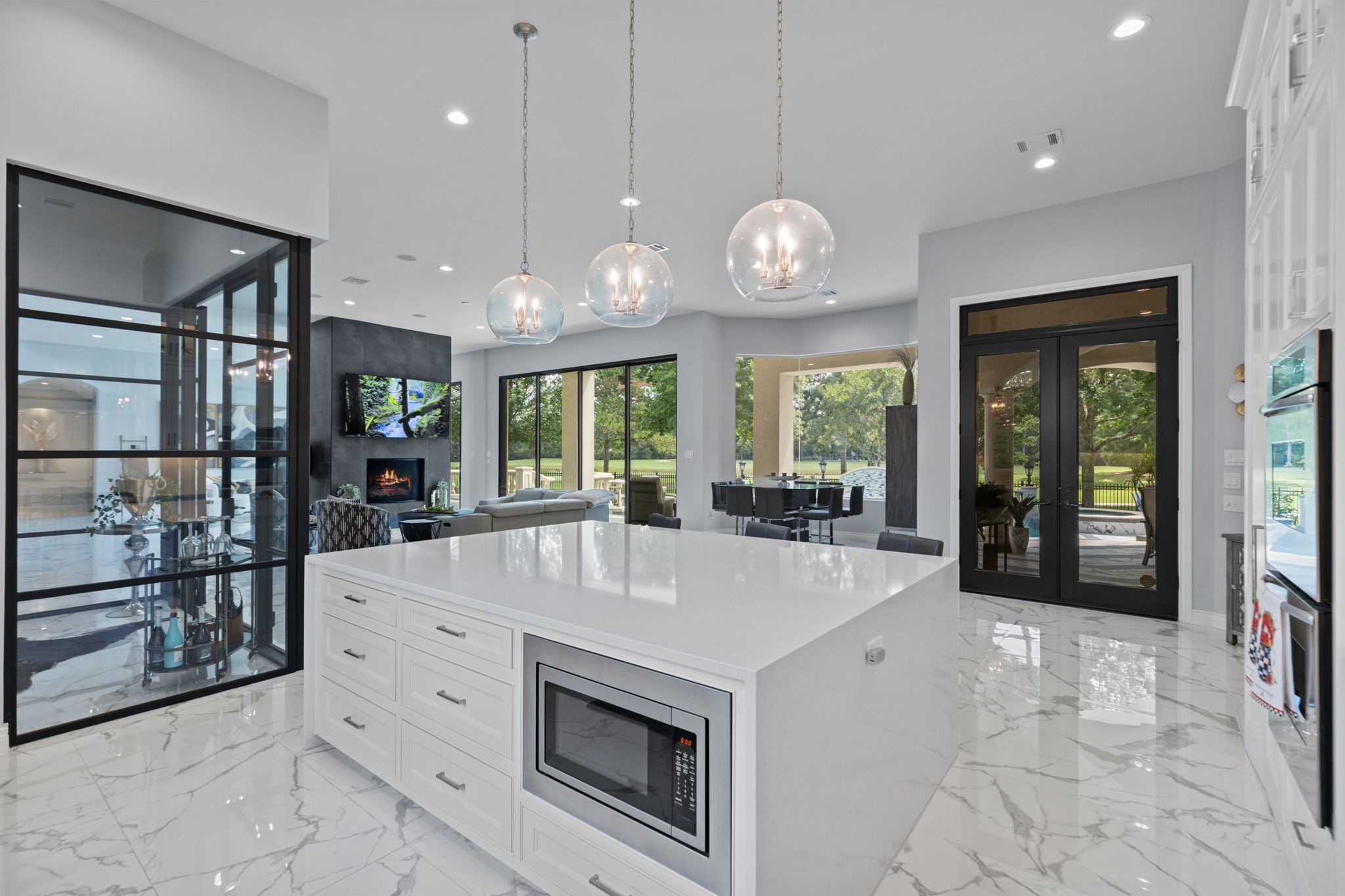39 Maymont Way Spring, TX 77382 - Photo 14 of 50 This modern kitchen features a spacious island with built-in microwave, sleek pendant lighting, and glossy marble flooring. Large glass doors and windows provide abundant natural light and views of the outdoor greenery.