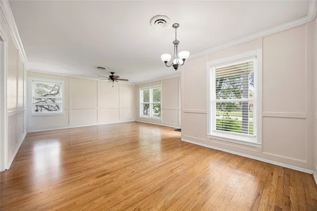 an empty room with wooden floor chandelier and windows