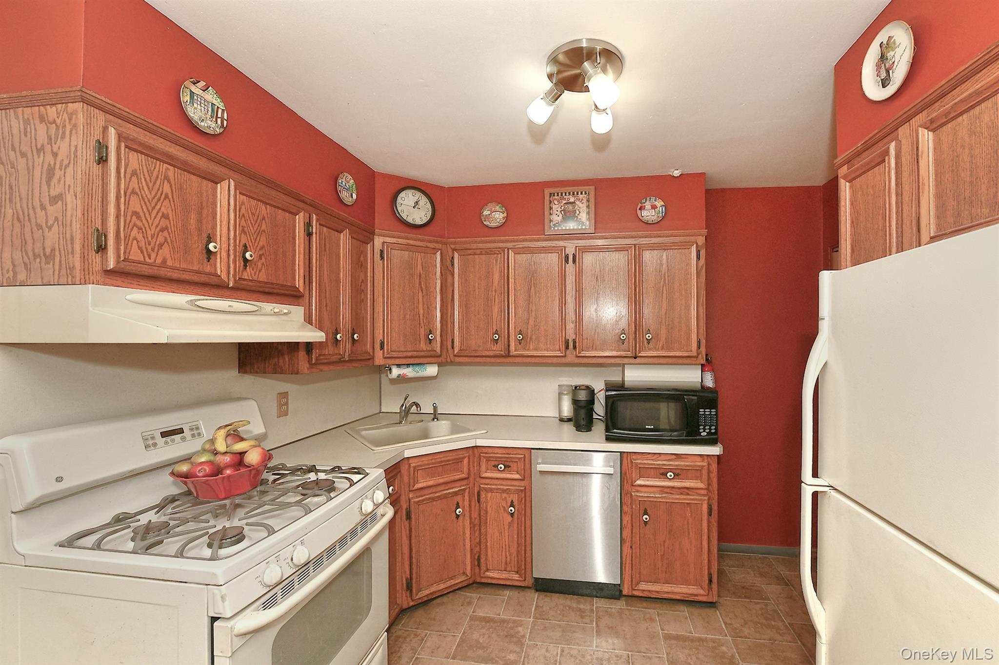 63-05 138th Street Queens, NY 11367 - Photo 10 of 22 Kitchen with white appliances, light countertops, under cabinet range hood, and brown cabinets