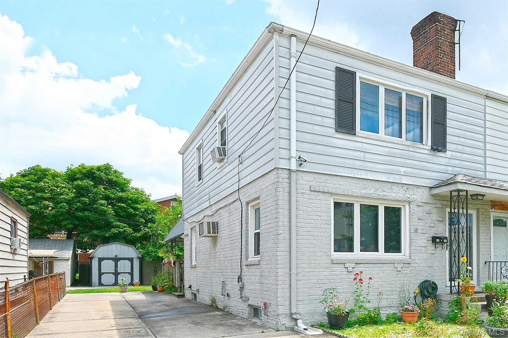 63-05 138th Street Queens, NY 11367 - Photo 2 of 22 View of side of property with a storage unit, brick siding, a chimney, and driveway