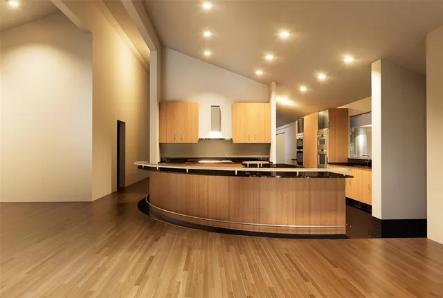 a view of empty room with wooden floor and kitchen