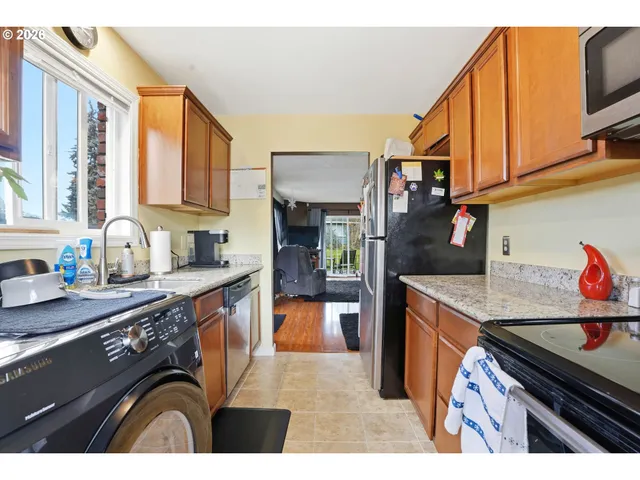 a kitchen with stainless steel appliances granite countertop a refrigerator a sink dishwasher a stove and a dining table with wooden floor