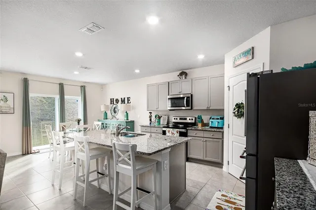 a kitchen with stainless steel appliances a dining table chairs refrigerator and microwave