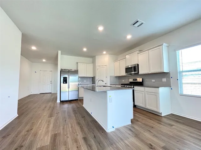 a kitchen with stainless steel appliances granite countertop a sink dishwasher a refrigerator and a stove with wooden floor